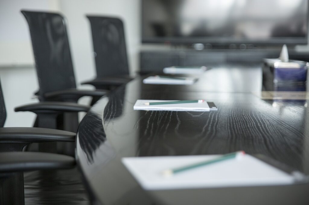 Mesa de juntas con sillas ergonómicas de oficina y libretas con lápices listas para una reunión corporativa.
